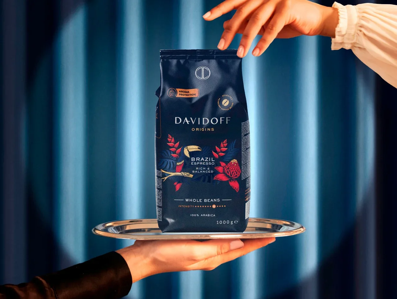 Ruky držia strieborný podnos s balíčkom kávy Davidoff Origins Brazil.