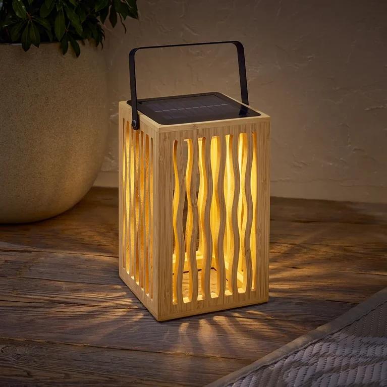 Dřevěná solární lampa s černou rukojetí stojí na dřevěném stole vedle květináče s rostlinou.