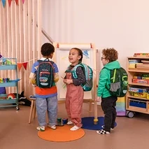 Tri deti stoja v miestnosti s batohmi a maľujú na plátno.