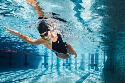 Žena pláva pod vodou v bazéne v čiernych plavkách arena Feel Lily Swim Pro Back s vystuženými košíčkami.