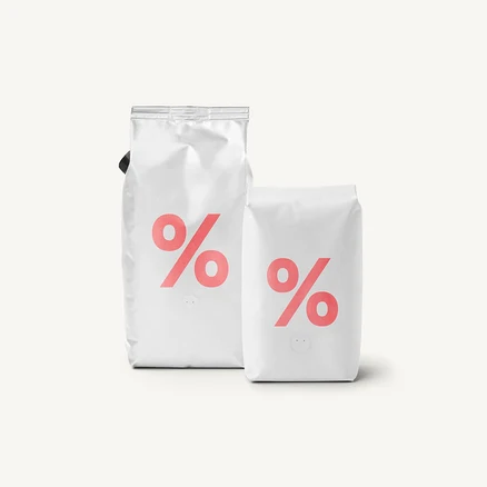 Dve biele vrecká kávy s ružovým logom percent na svetlom pozadí.
