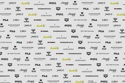 Svetlé pozadie s opakujúcim sa vzorom rôznych log značiek, vrátane Lurchi, seidensticker, ANGELS, sloggi, Steiff, SCHIESSER, hummel, ROMIKA, PASSIONATA, arena, TOM TAILOR, FILA, CMP a JAKO-O.