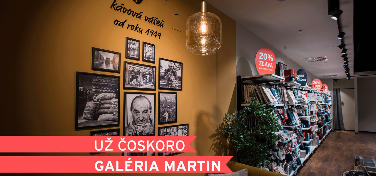 Interiér obchodu so žltou stenou, na ktorej sú čiernobiele fotografie a text „kávová vášeň od roku 1949“. Sklenené závesné svietidlo visí nad žltou pohovkou s vankúšmi a bielym stolíkom. V pozadí sú regály s produktmi a červené nápisy „20% ZĽAVA“. Červený banner hlása „UŽ ČOSKORO GALÉRIA MARTIN“.