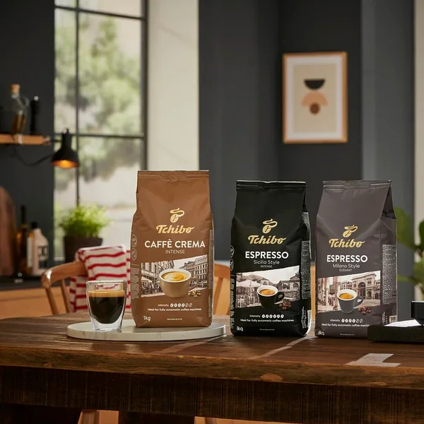 Kávovar pripravuje kávu do dvoch pohárov vedľa balení zrnkovej kávy Tchibo Caffè Crema, Espresso Sicilia Style a Espresso Milano Style.