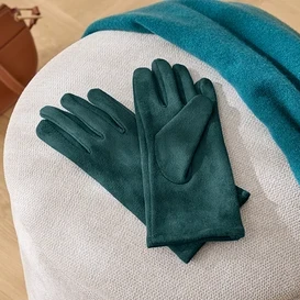 Na bielej stoličke ležia zelené rukavice, modrá šála a hnedá kabelka.