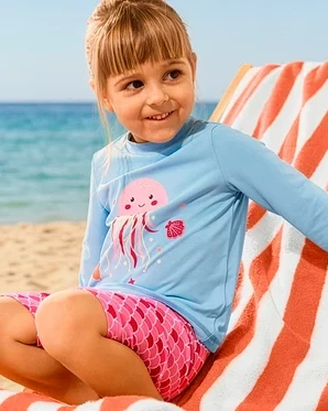 Dievča sedí na ležadle s XL osuškou a má na sebe Kinder-Kombi mit UV-Schutzfaktor 50+, Qualle.