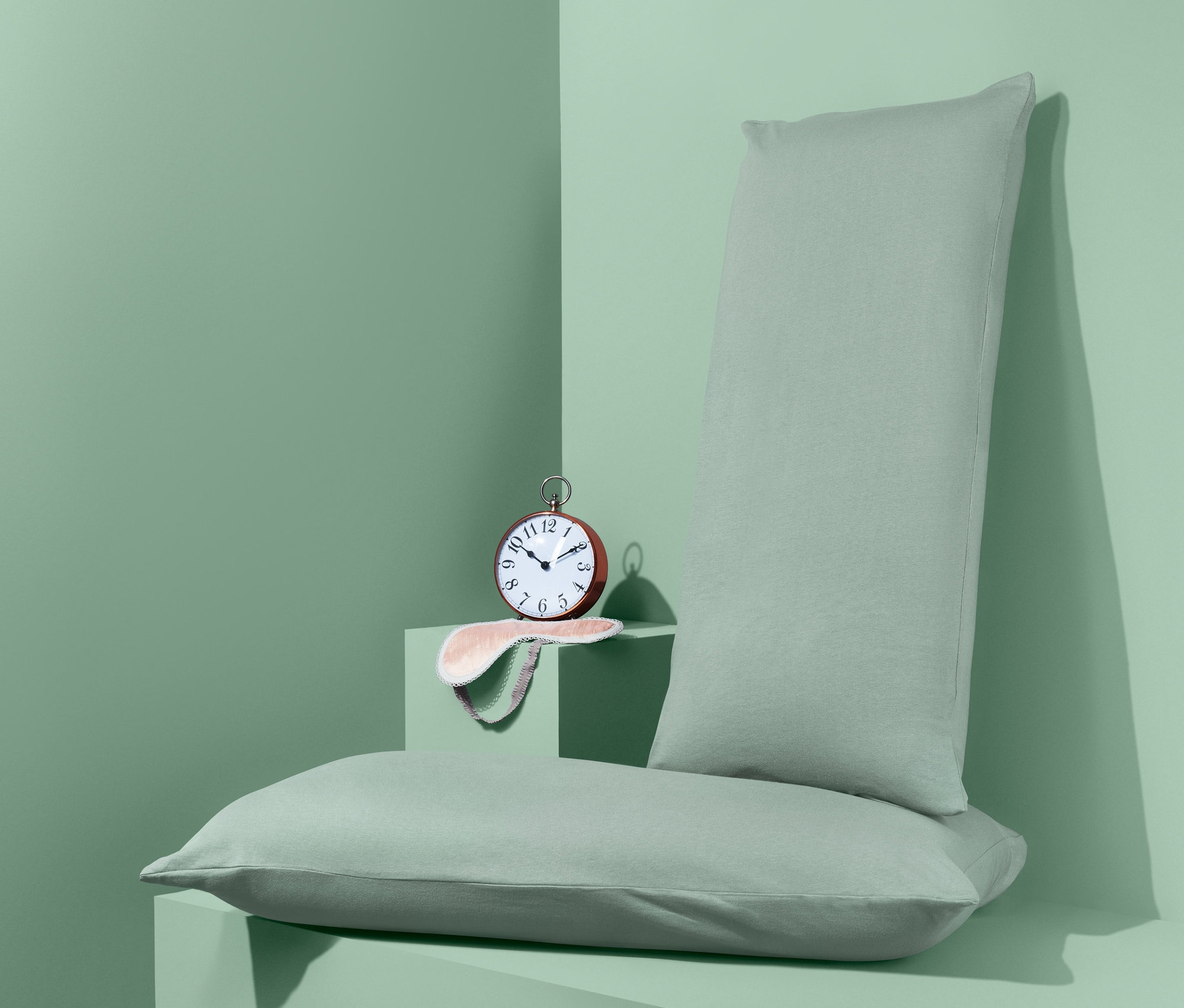 Dve džersejové obliečky na vankúše a budík ležia na sebe na zelenom pozadí.