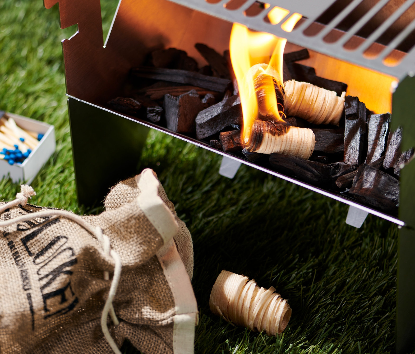 Horľavé podpaľovače uhlia na gril v grile. Vedľa grilu ležia zápalky a vrece s podpaľovačmi.