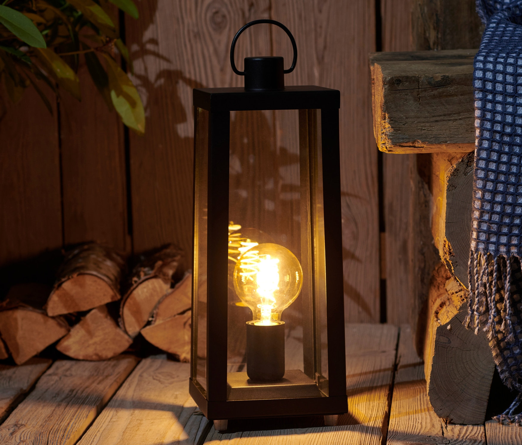 Čierna záhradná lampa s LED na drevenej podlahe.