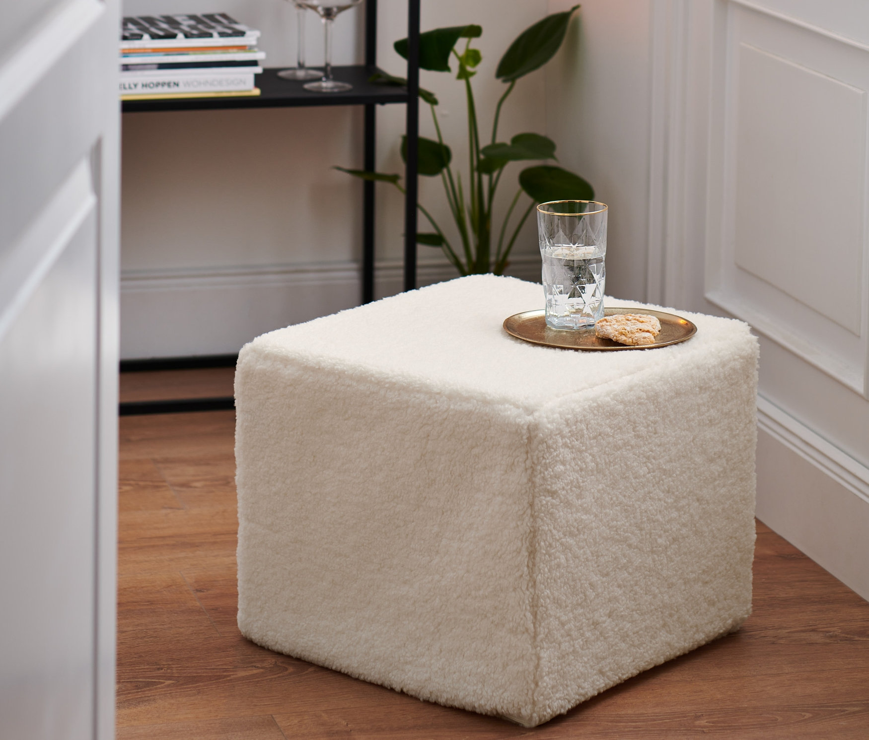 Biely taburet stojí na drevenej podlahe. Na taburete je pohár vody a sušienka.