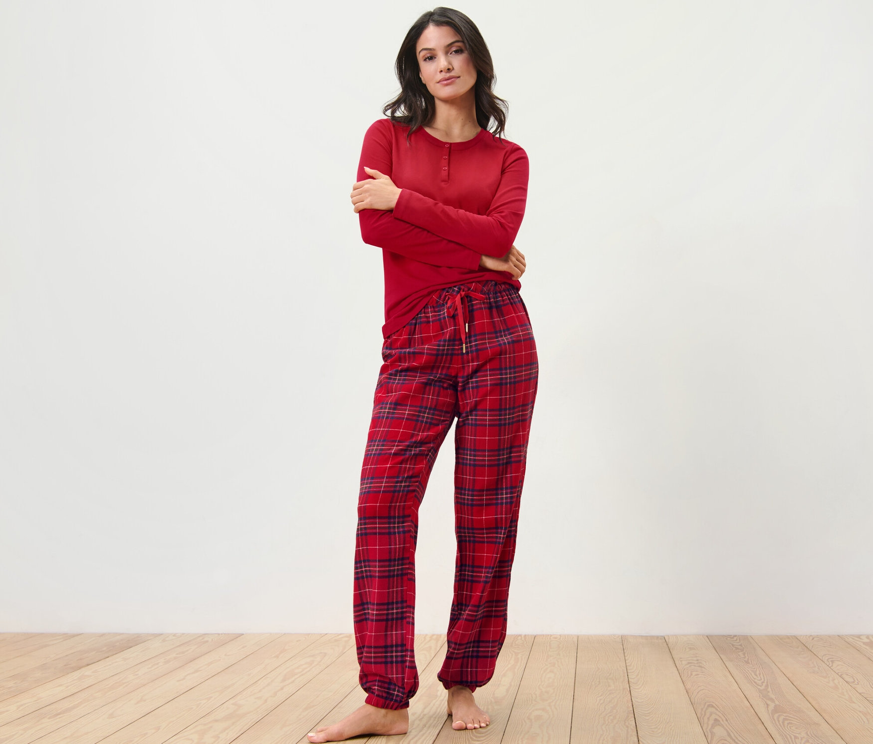 Žena pózuje v červenom flanelovom pyžame s károvaným vzorom.