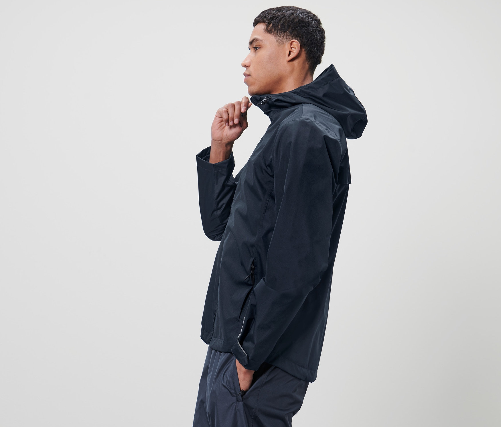 Muž si zapína modrú unisexovú bundu do dažďa.