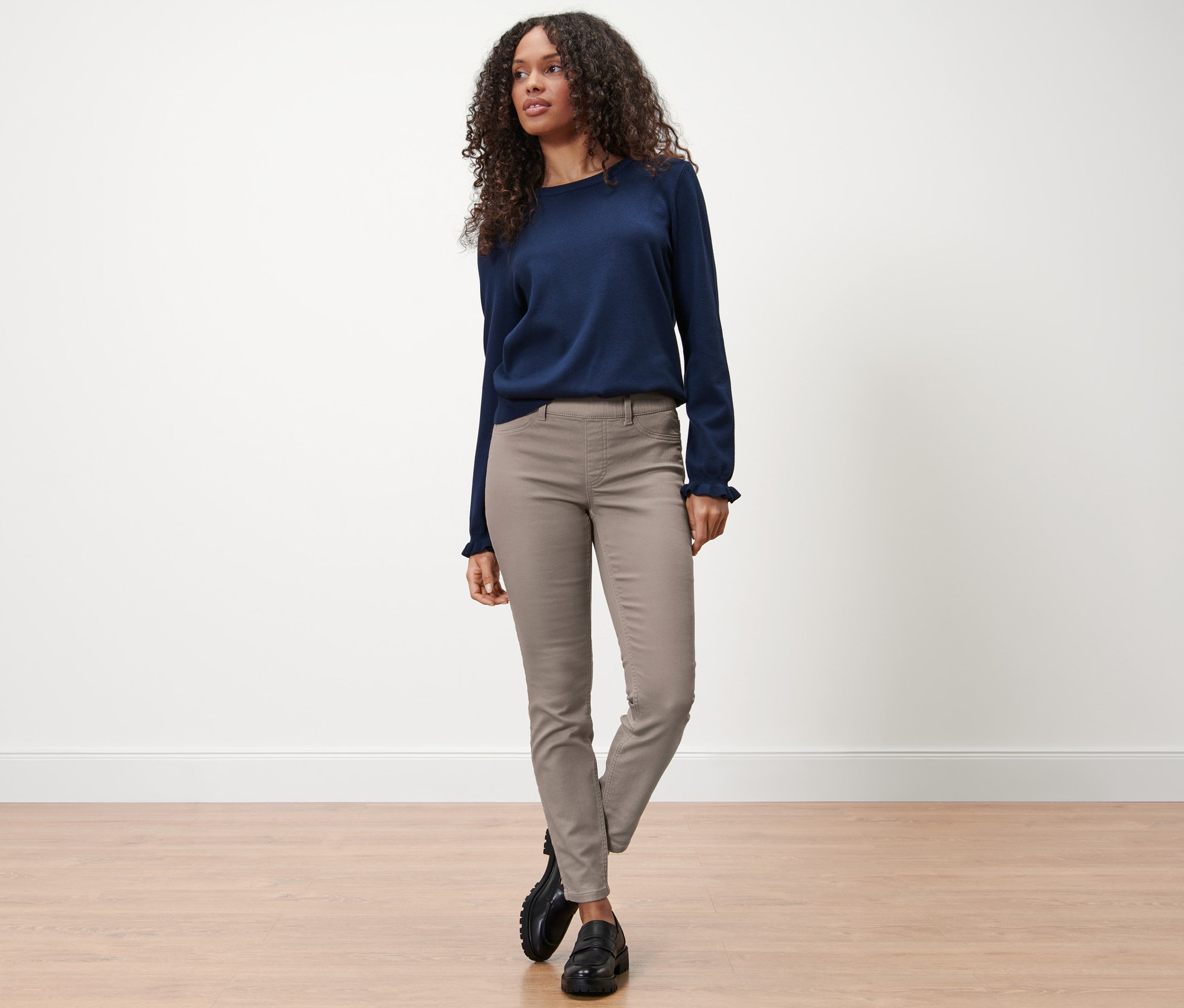 Žena stojí na podlahe v hnedosivých tregínsoch »Nelly« a modrom svetri.