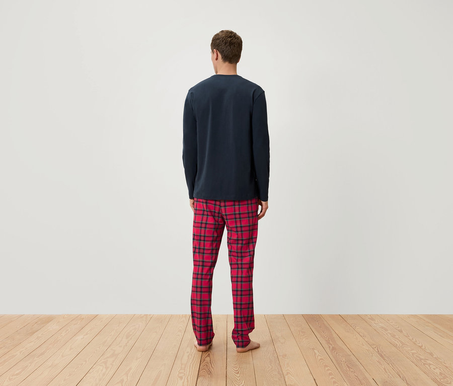 Muž chrbtom k fotoaparátu má na sebe tmavomodré pyžamové tričko s dlhým rukávom a červené kárované pyžamové nohavice.