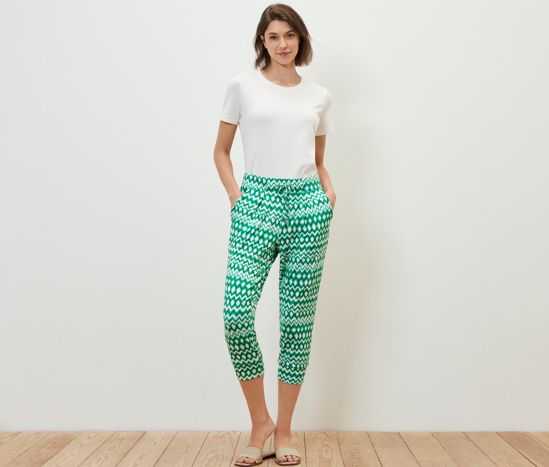 Žena stojí s rukami vo vreckách v trojštvrťových džersejových nohaviciach s potlačou.