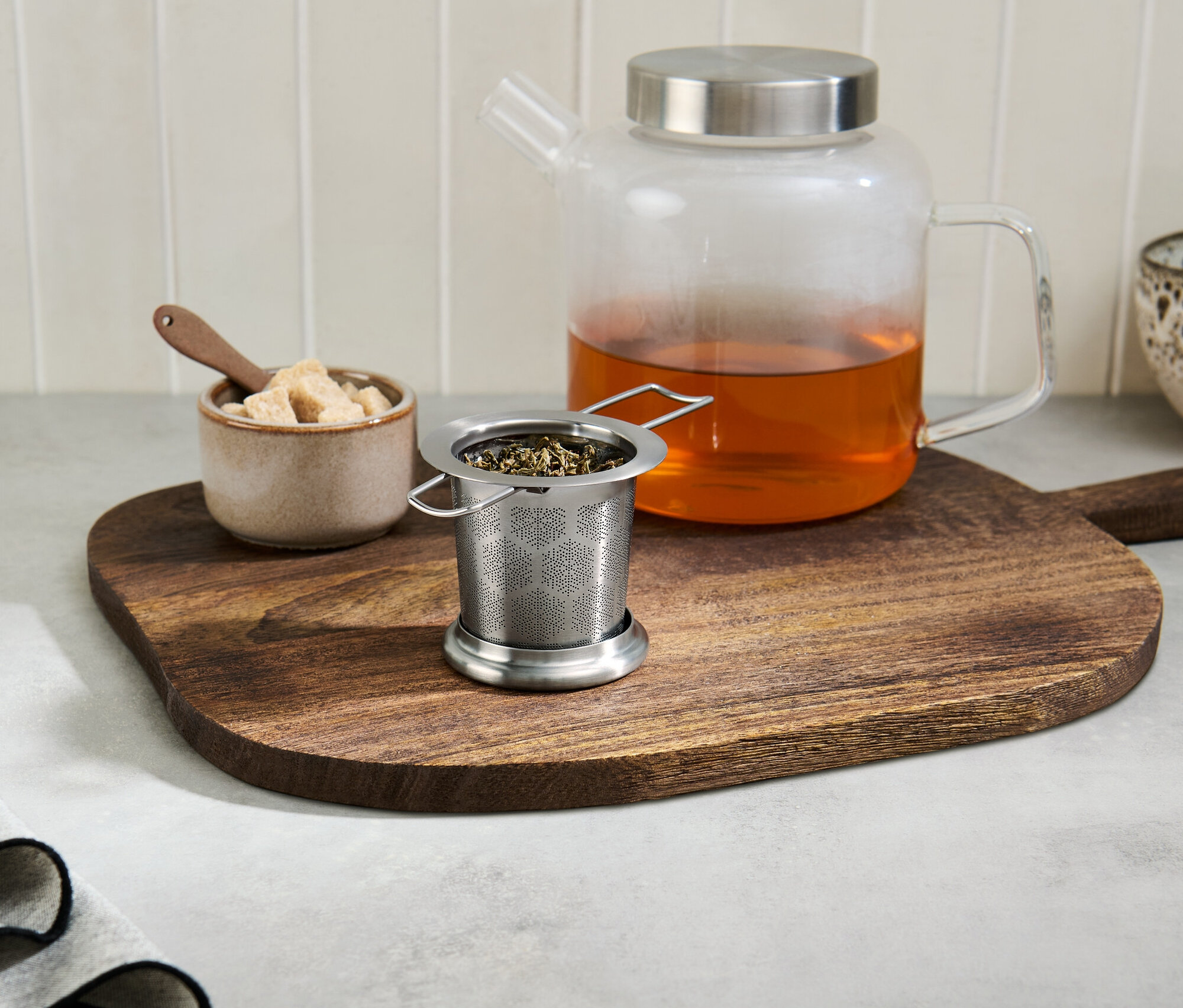 Sitko na čaj s čajom na drevenej doske vedľa sklenenej kanvice s čajom.