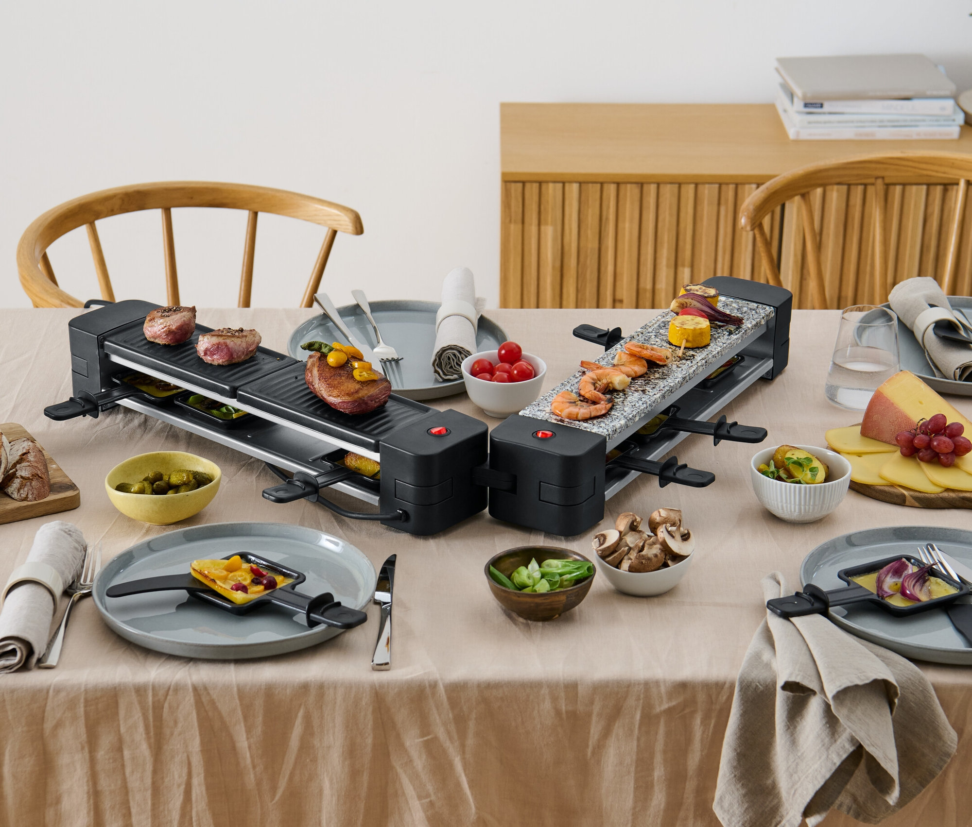 Dva sklopné raclette grily s jedlom na stole.