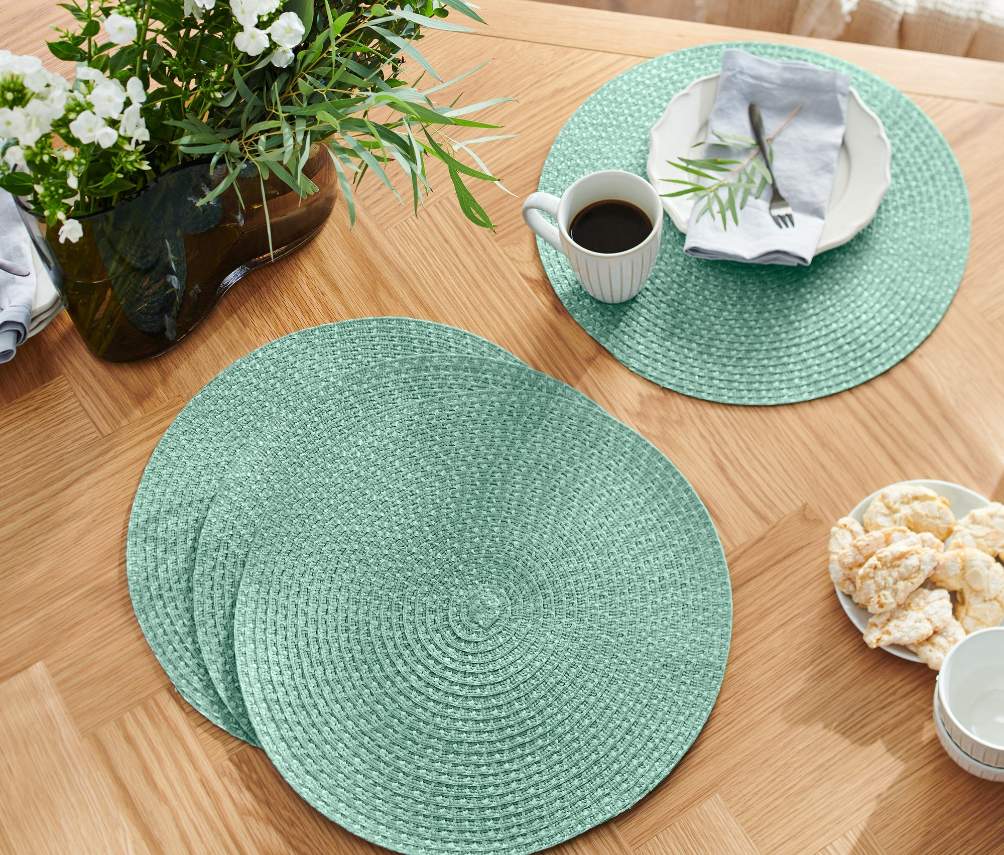 Na drevenom stole ležia štyri zelené prestierania.