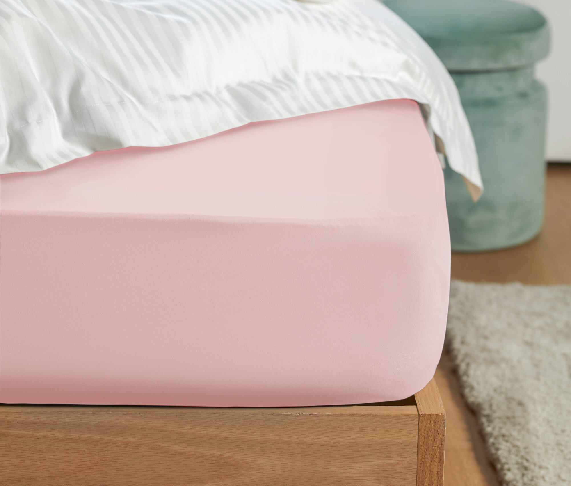 Detail ružovej plachty na posteli s bielymi pruhovanými obliečkami a zelenou stoličkou v pozadí.