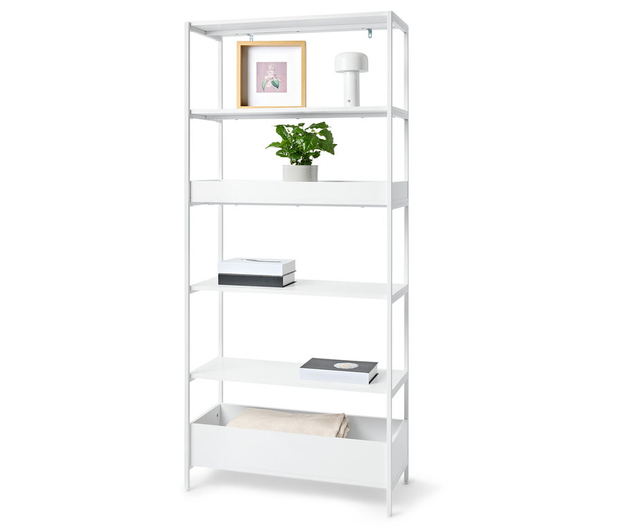 Biela knižnica s piatimi policami s rastlinou, rámom s obrázkom, lampou, dvoma krabicami a dekou.