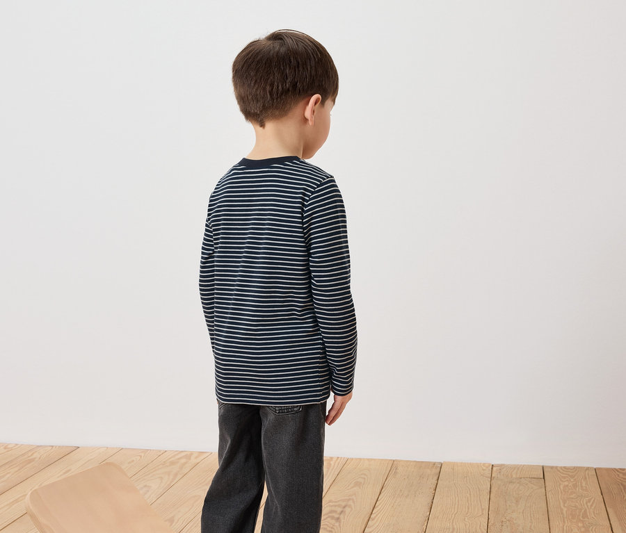 Chlapec stojí chrbtom a má na sebe pruhované tričko s dlhým rukávom a džínsy.