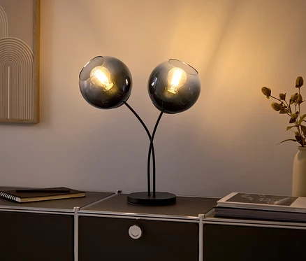Dve sklenené lampy so žiarovkami na čiernej komode.