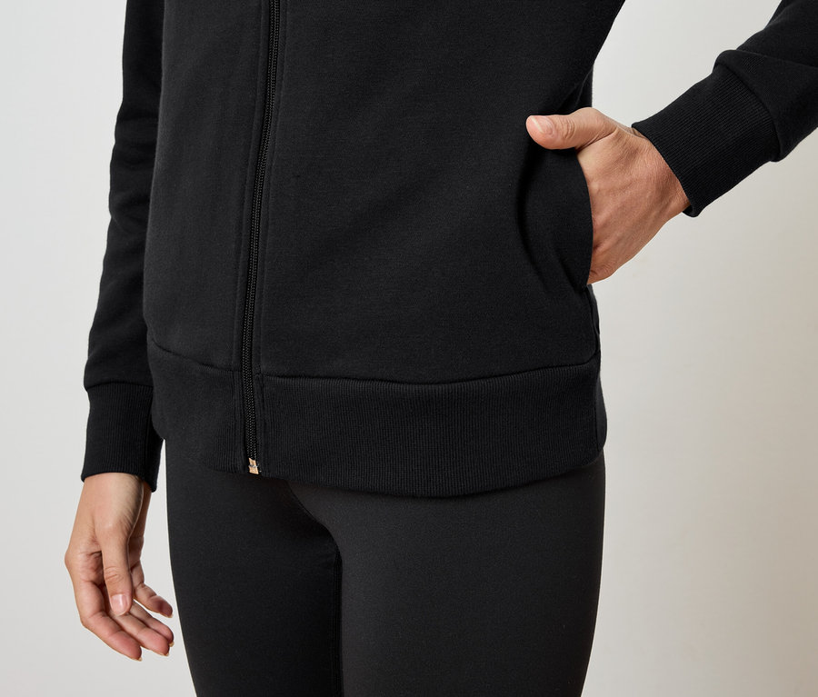 Žena má ruku vo vrecku čiernej mikiny na zips a má na sebe čierne legíny.