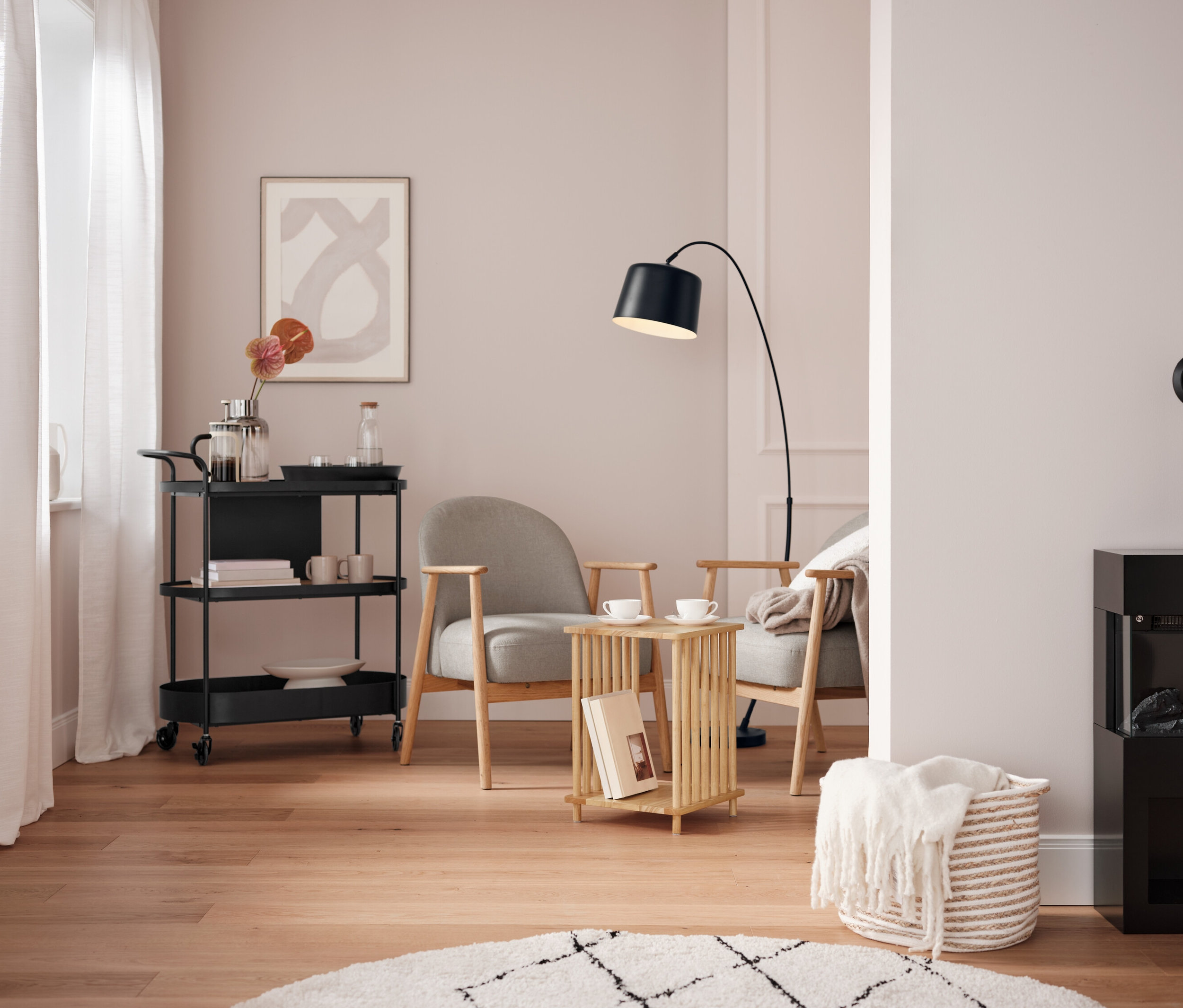 Obývacia izba s čiernym servírovacím vozíkom, dvoma sivými kreslami a čiernym krbom.