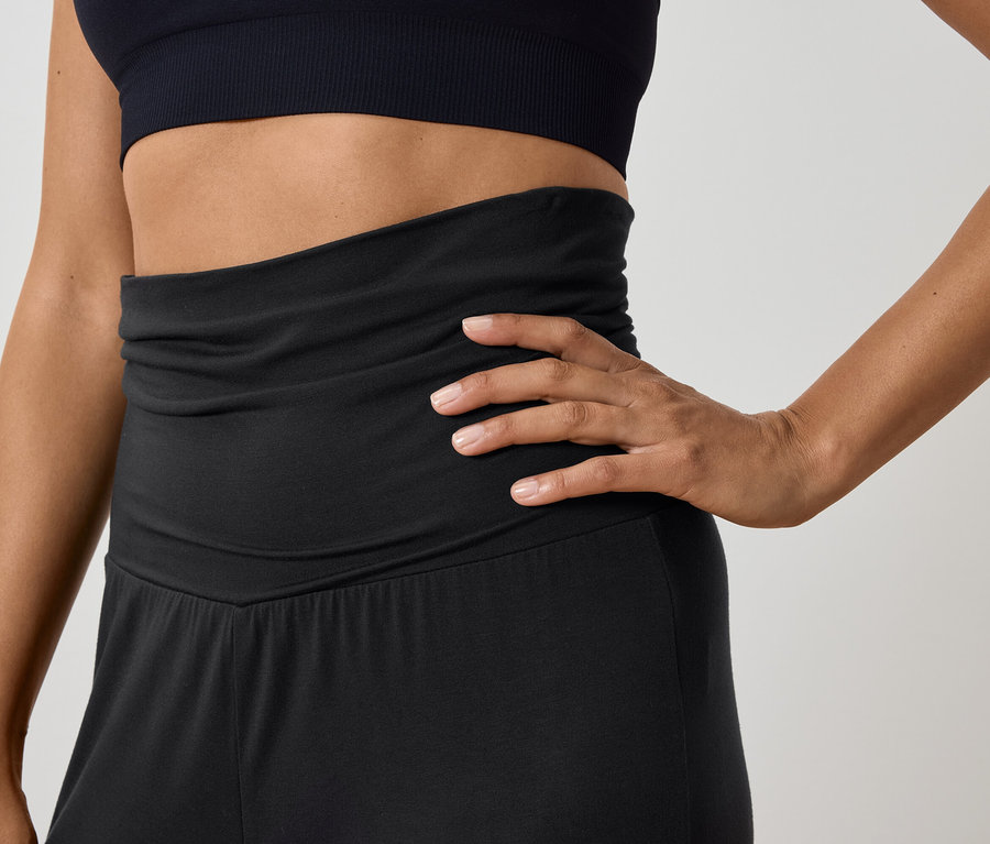 Žena pózuje v čiernom športovom tope a nohaviciach s vysokým pásom.