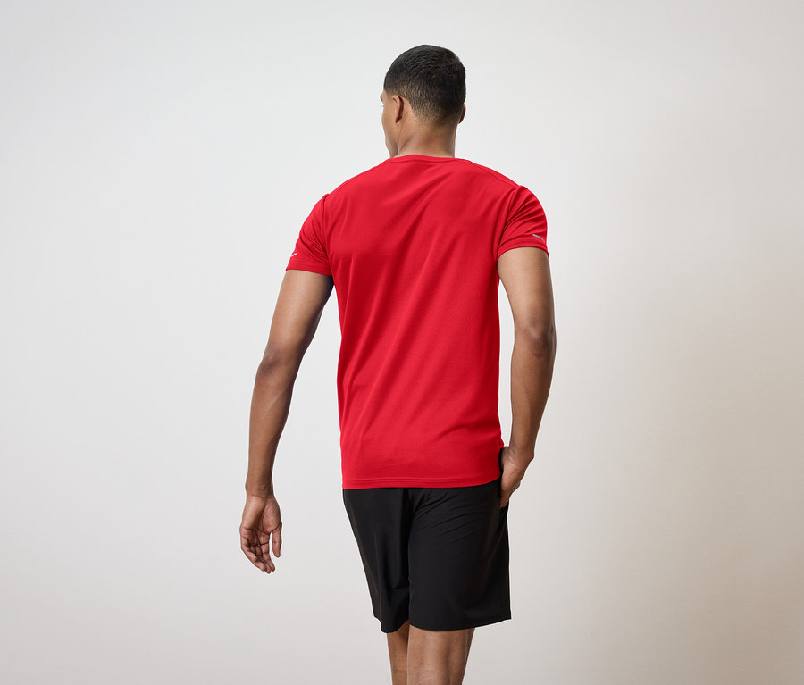 Muž chrbtom k fotoaparátu má na sebe červené tričko a čierne šortky.