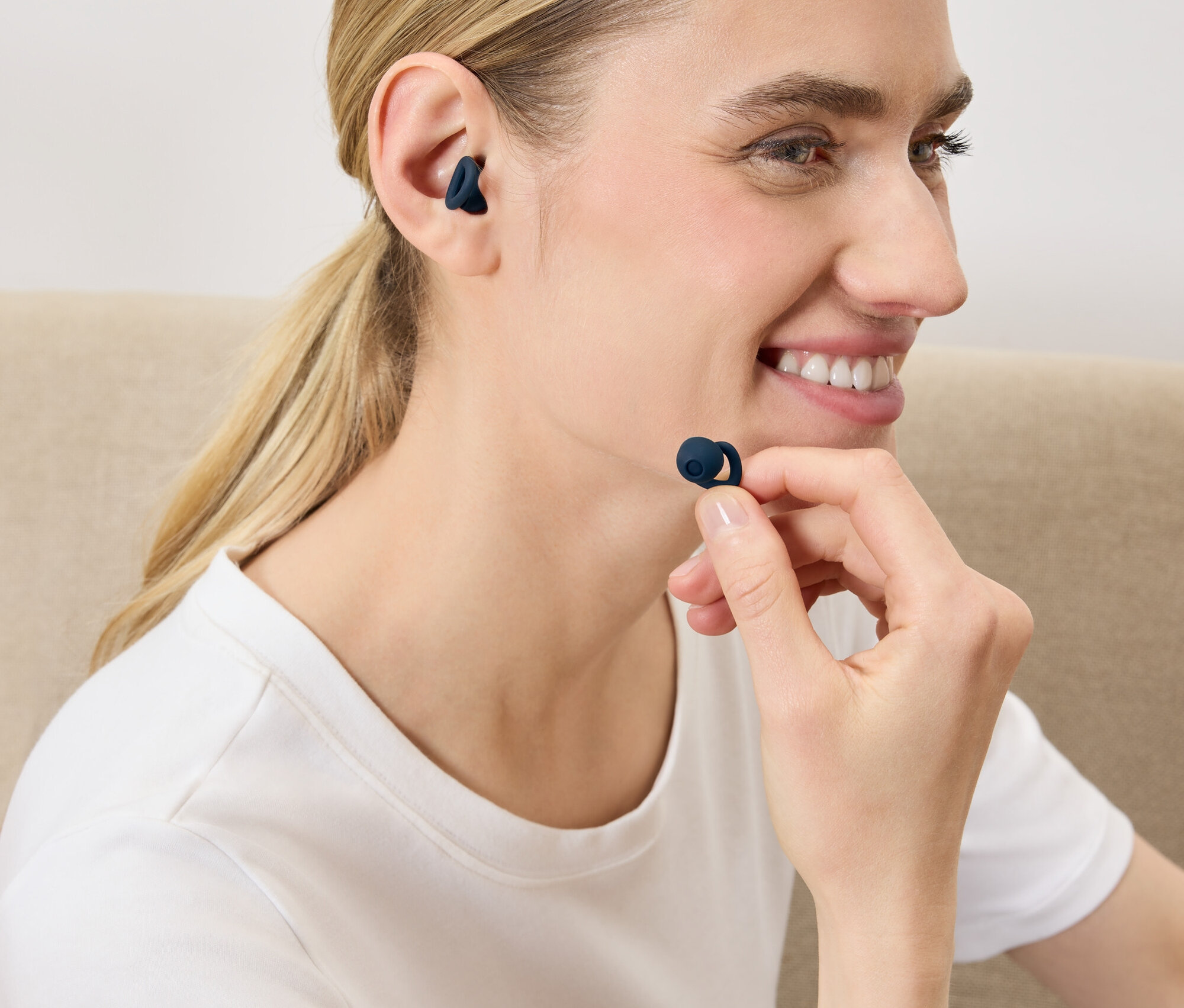 Žena si vkladá do ucha tmavomodré bezdrôtové slúchadlo.