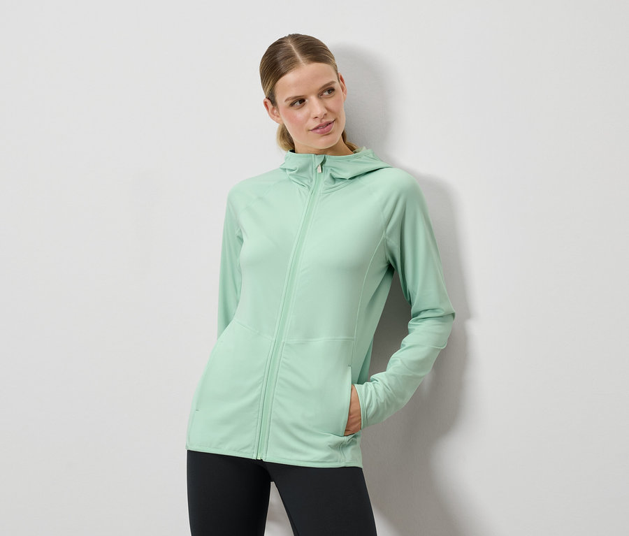 Žena pózuje v mätovo zelenom svetri s kapucňou a čiernych legínach.