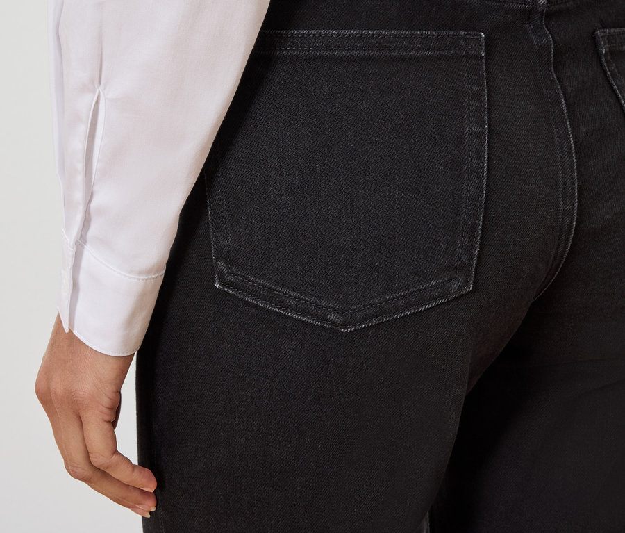 Detail zadnej časti čiernych džínsov na osobe, ktorá má na sebe bielu košeľu.