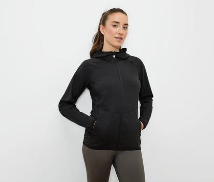 Žena má ruky vo vreckách čiernej športovej bundy s kapucňou na zips.