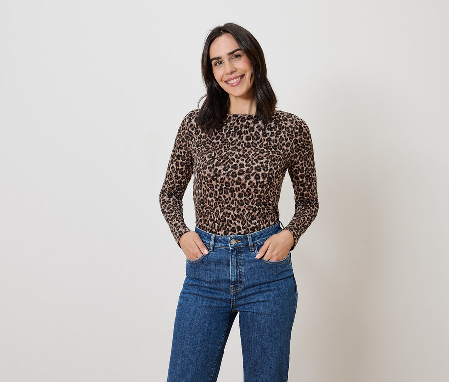 Žena s hnedými vlasmi pózuje v tope so zvieracou potlačou a modrých džínsoch.