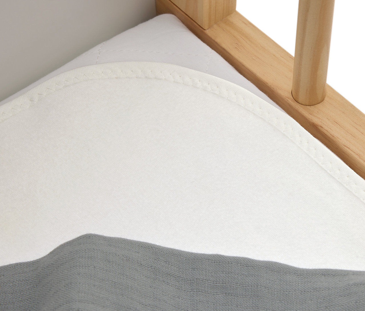 Detailný záber na biely matrac so sivou látkou na drevenej posteli.