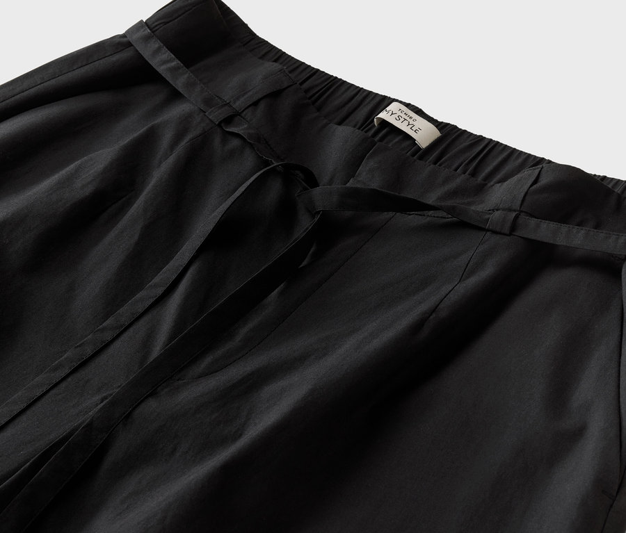Detailný záber na čierne nohavice so zaväzovacím opaskom a štítkom s nápisom "TCHINO MY STYLE".