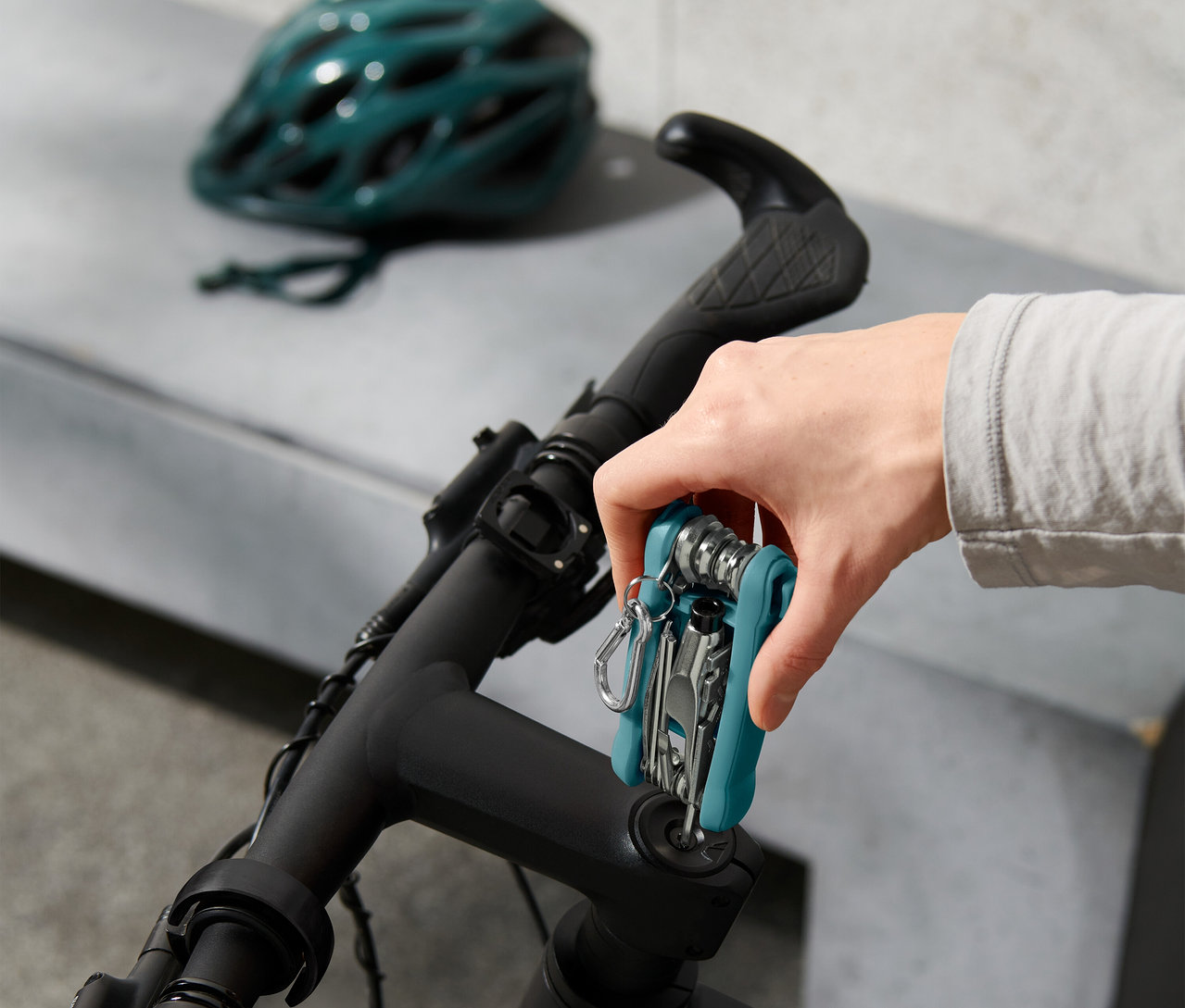 Ruka pripevňuje multifunkčné náradie na riadidlá bicykla, v pozadí cyklistická prilba.