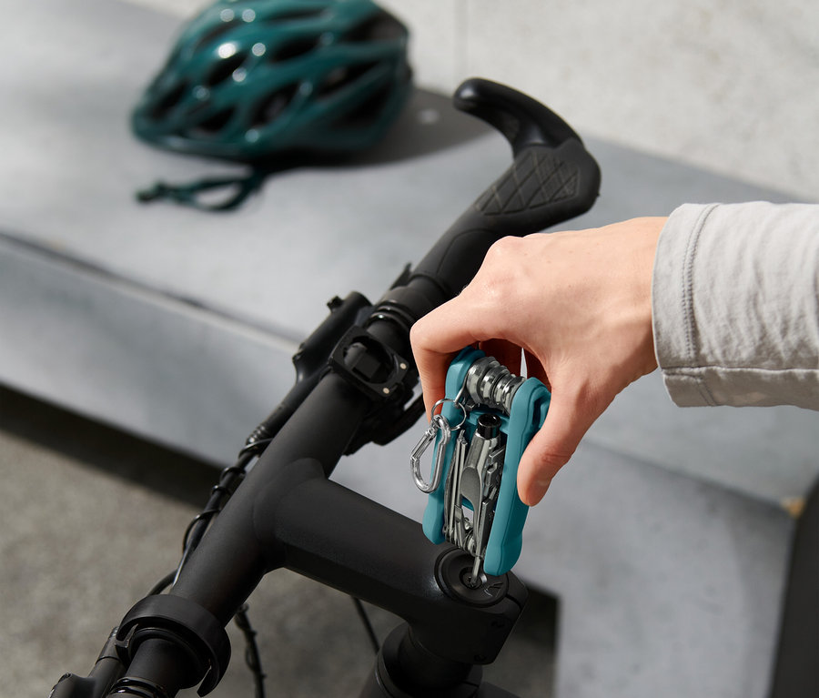 Ruka pripevňuje multifunkčné náradie na riadidlá bicykla, v pozadí cyklistická prilba.