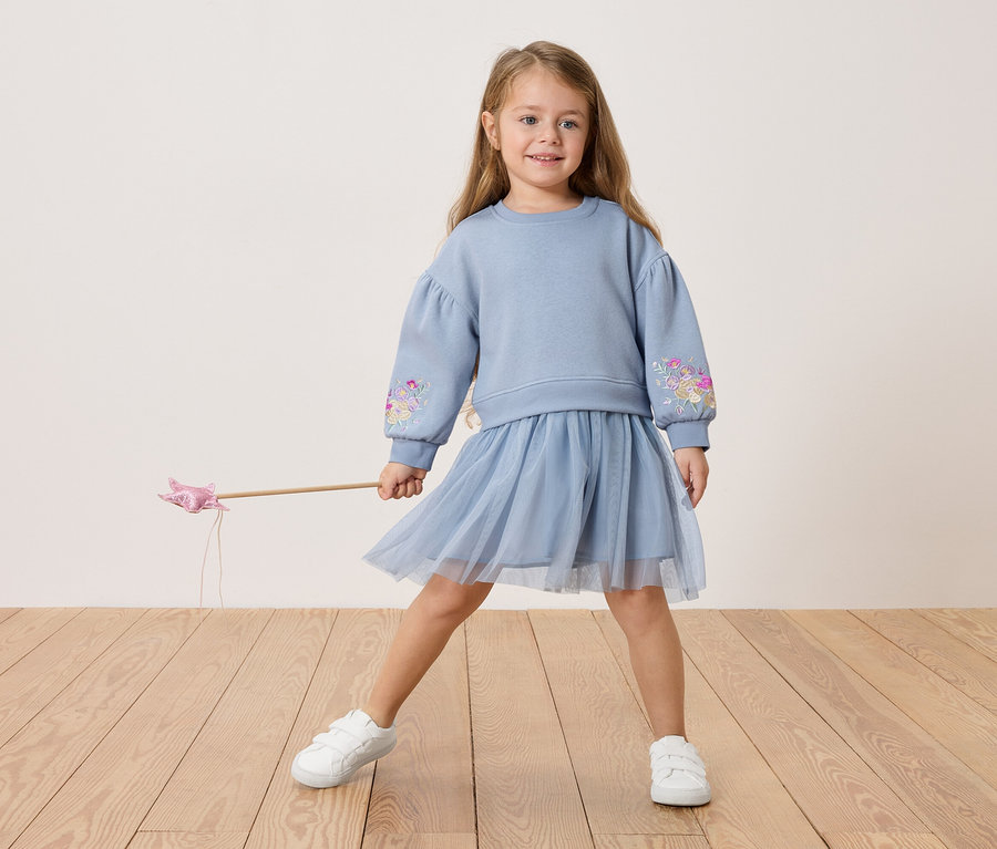 Dievča v modrej blúze s kvetinovou výšivkou a tylovej sukni, drží prútik.