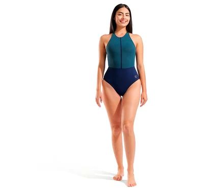 Usmievavá žena stojí v dámskych plavkách arena Shapewear Silvia B-Cup Cross Back. Jednodielne plavky sú hore tyrkysové so zipsom a dole tmavomodré.