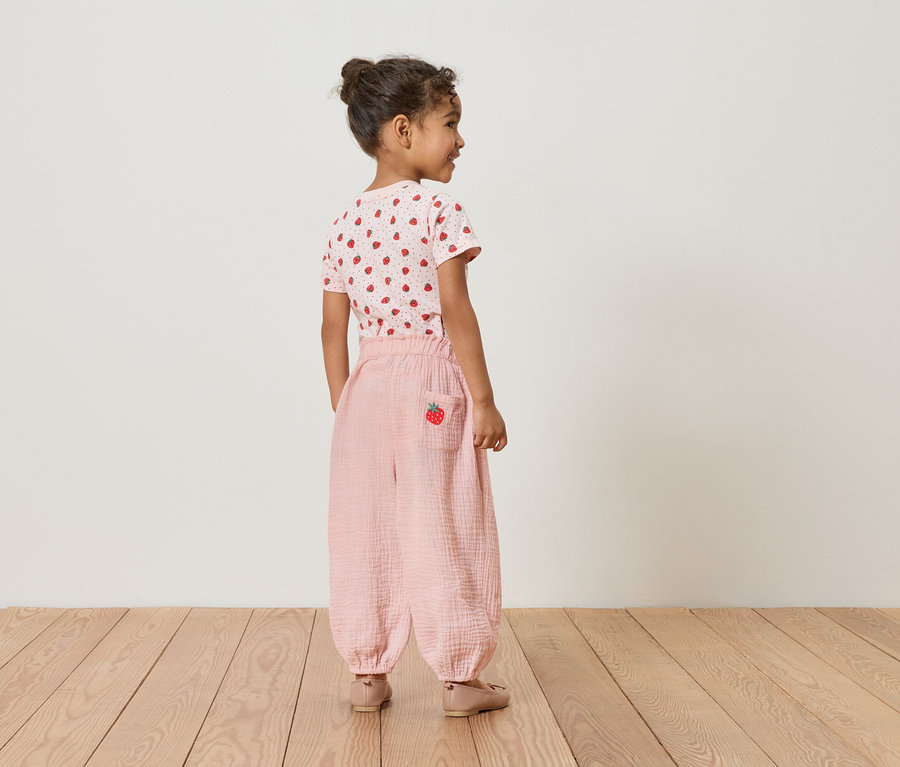 Dievča zozadu, má na sebe jahodové tričko a ružové nohavice s jahodovým detailom.