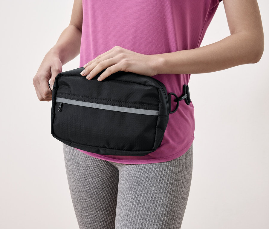 Žena s čiernou bedrovou taškou s reflexným pruhom.