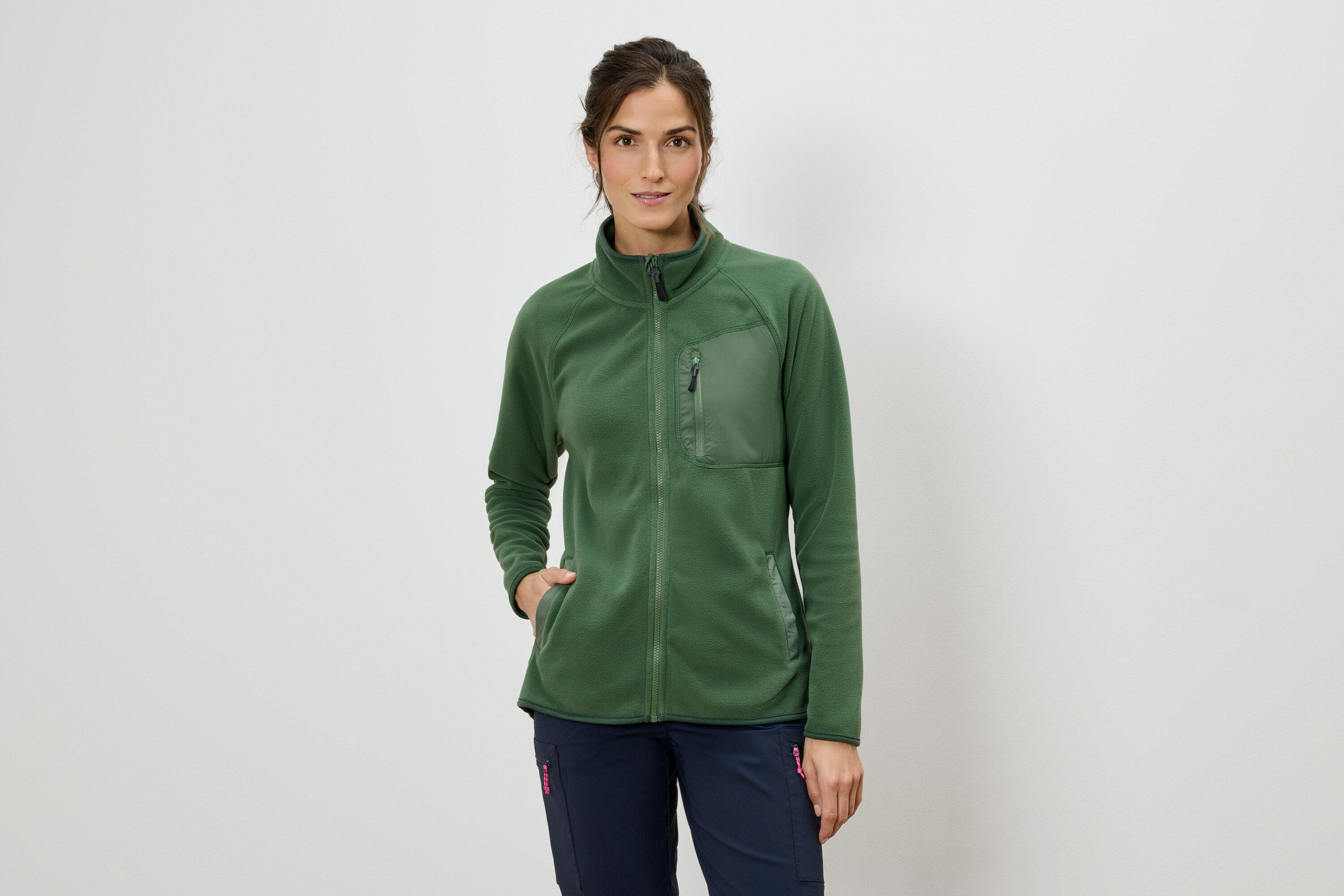 Žena v zelenej flísovej bunde na zips a modrých nohaviciach.