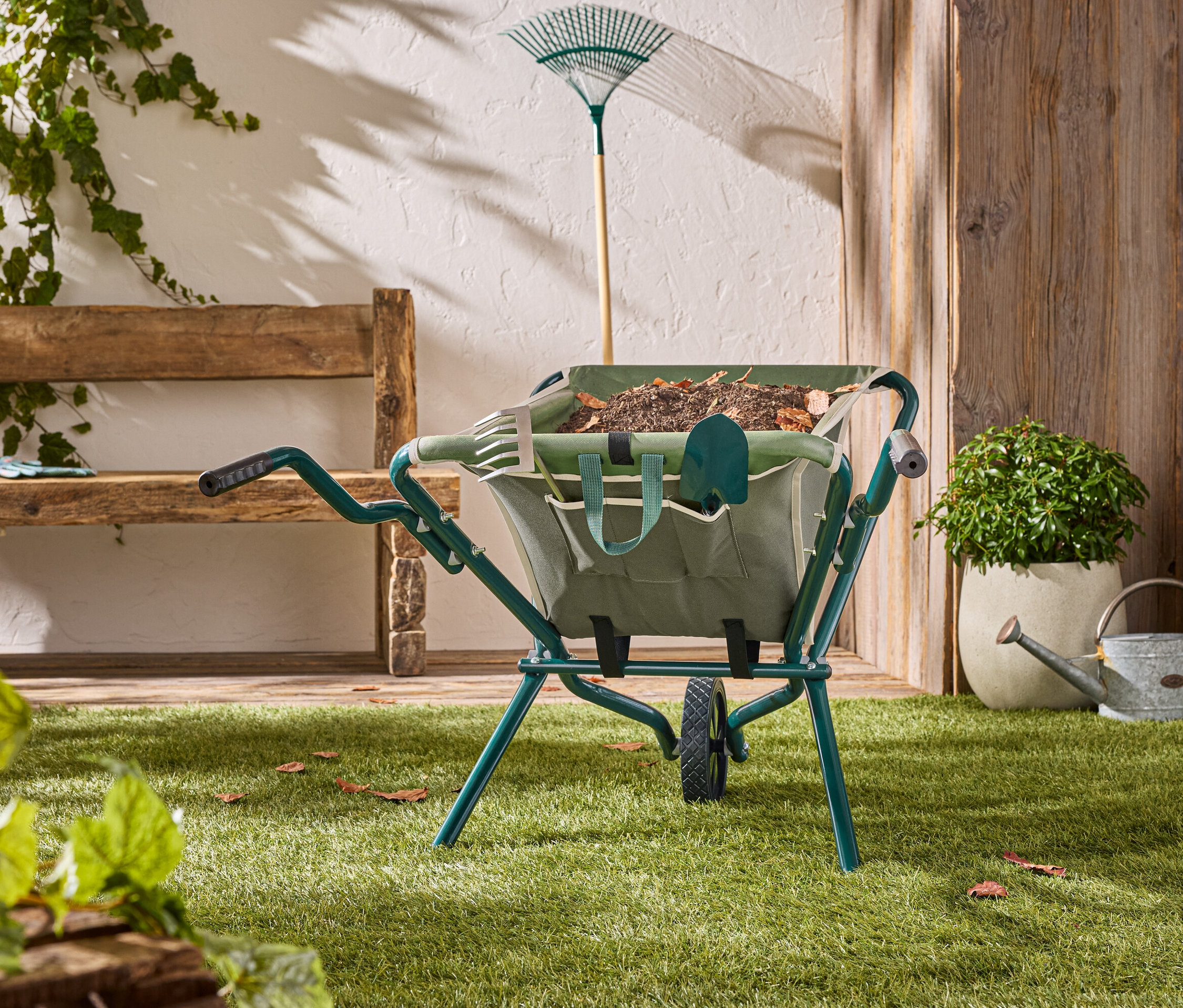 Zelený fúrik stojí na trávniku so záhradným náradím vnútri.