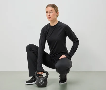 Žena v čiernom športovom oblečení čupí a oboma rukami drží 4 kg kettlebell.
