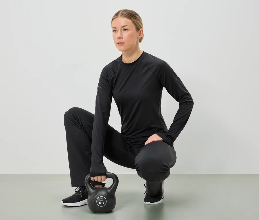 Žena v čiernom športovom oblečení čupí a oboma rukami drží 4 kg kettlebell.
