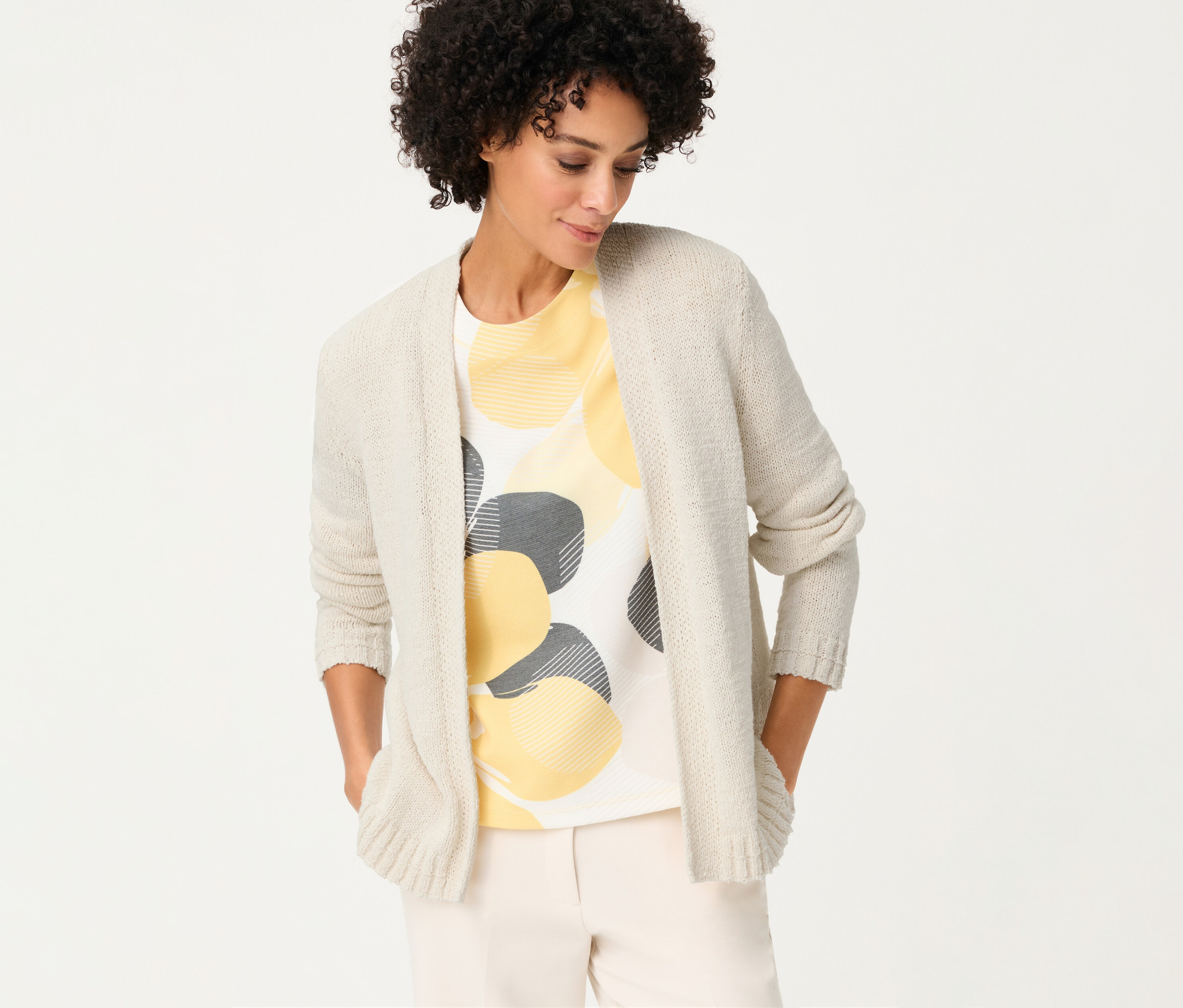 Žena s ľanovým kardigánom Olsen cez tričko so žltými a sivými kruhmi, má ruky vo vreckách.