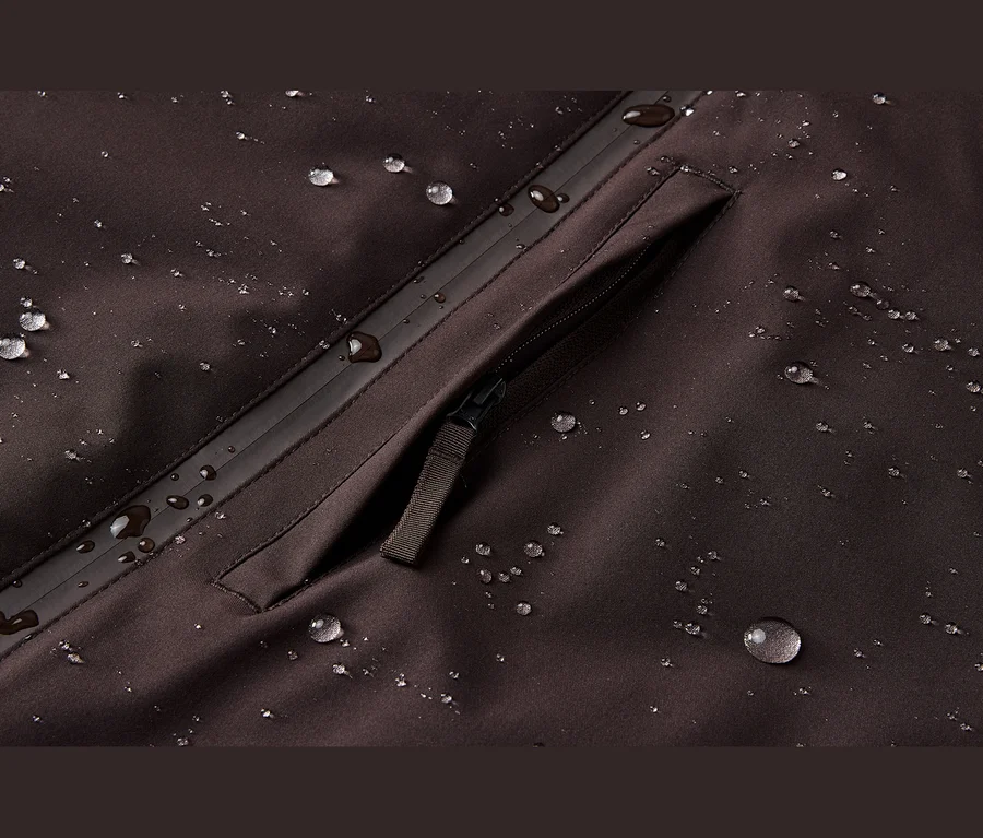 Detail tmavohnedej nepremokavej látky s kvapkami vody a vreckom na zips.