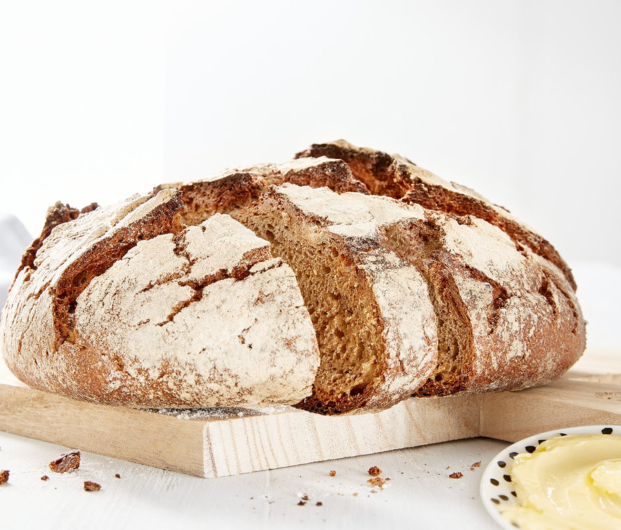 Bochník chleba na drevenej doske vedľa taniera masla.